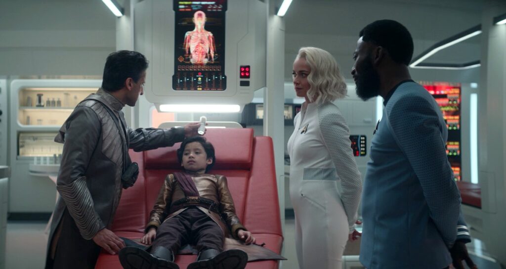 The First Servant of Majalas is tended to by his father, Gamal, in sickbay with Nurse Chapel and Dr. M'Benga watching