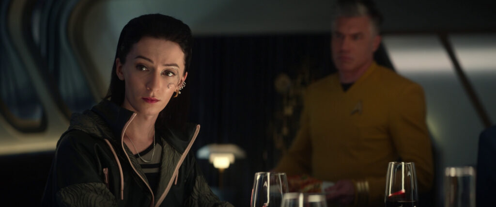 Jesse James Keitel as "Dr. Aspen" sitting at the dinner table with Captain Pike (Anson Mount) in the background